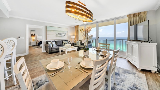 Een moderne woonkamer met een eethoek, grote ramen, een kroonluchter en uitzicht op de oceaan.