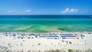 Een strand met rijen blauwe en witte ligbedden en parasols, helder turquoise water en een zandstrand.