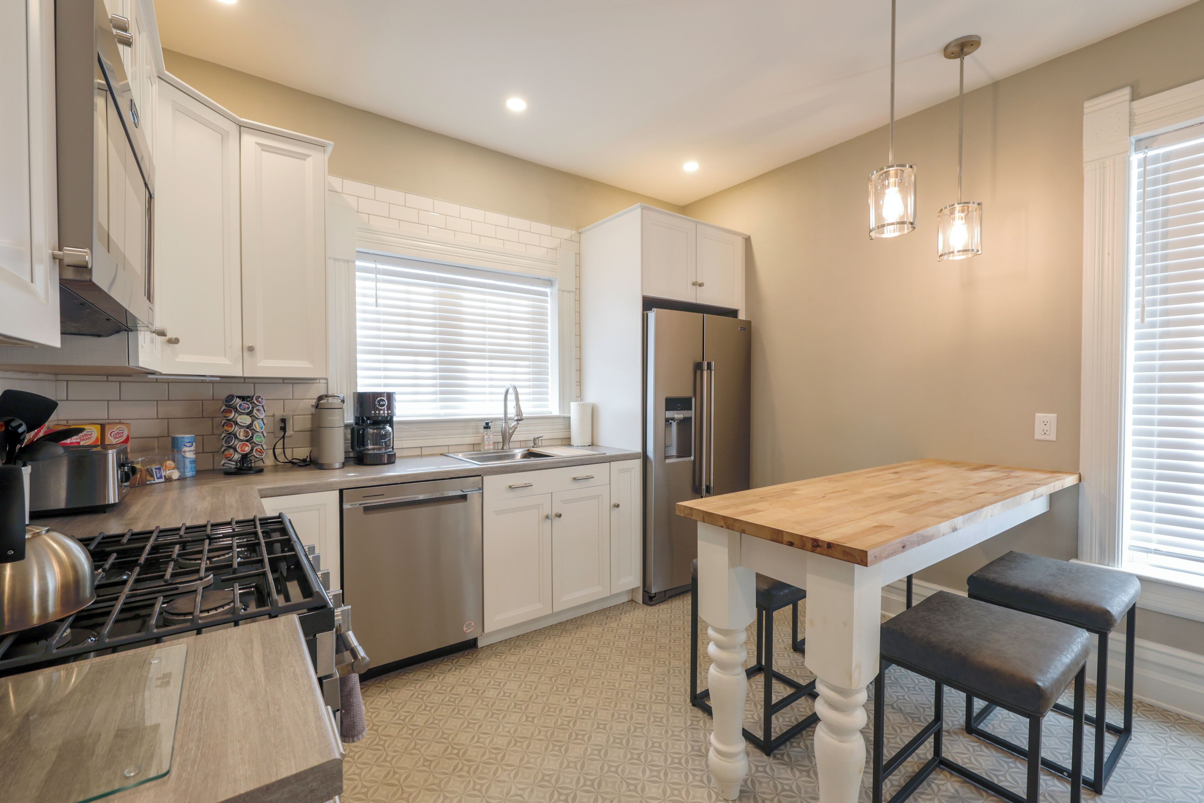 A kitchen with white cabinets, a stainless steel refrigerator, a wooden island, and pendant lights.