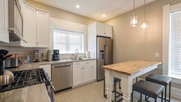 A kitchen with white cabinets, a stainless steel refrigerator, a wooden island, and pendant lights.