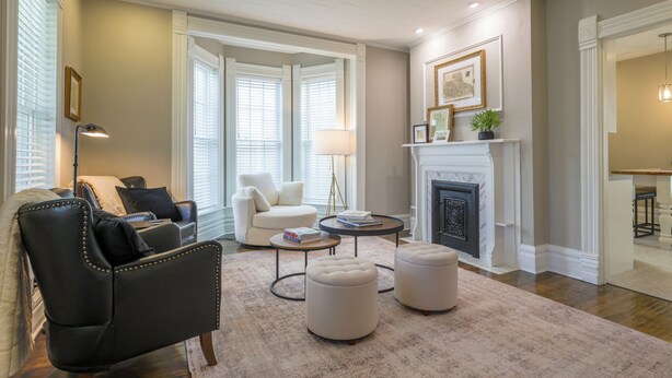 Una sala de estar con chimenea, un sillón de cuero negro, un sillón blanco y una mesa de centro redonda.