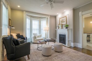 Una sala de estar con chimenea, un sillón de cuero negro, un sillón blanco y una mesa de centro redonda.
