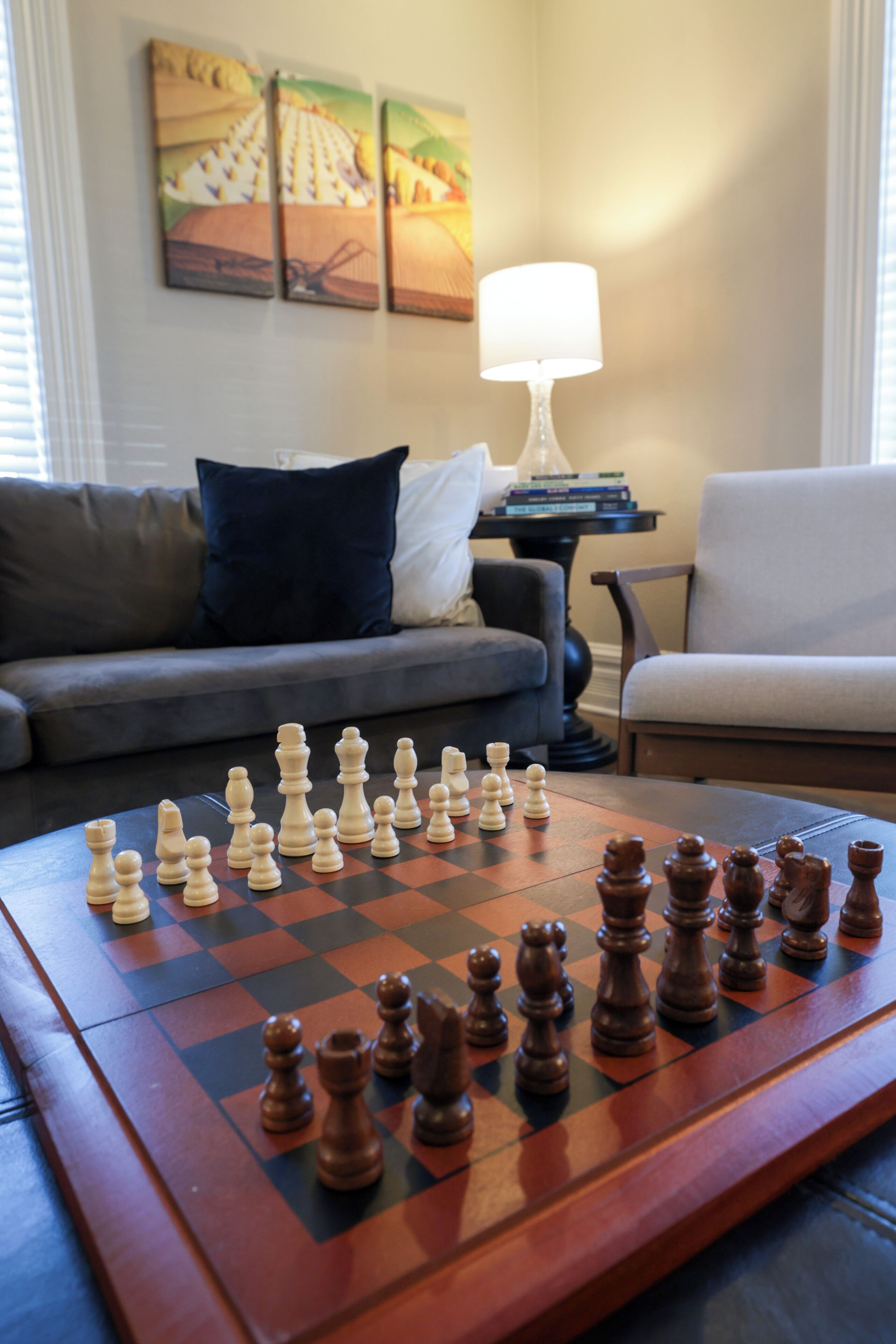 Un jeu d’échecs est posé sur une table dans un salon, avec un canapé et une lampe en arrière-plan.