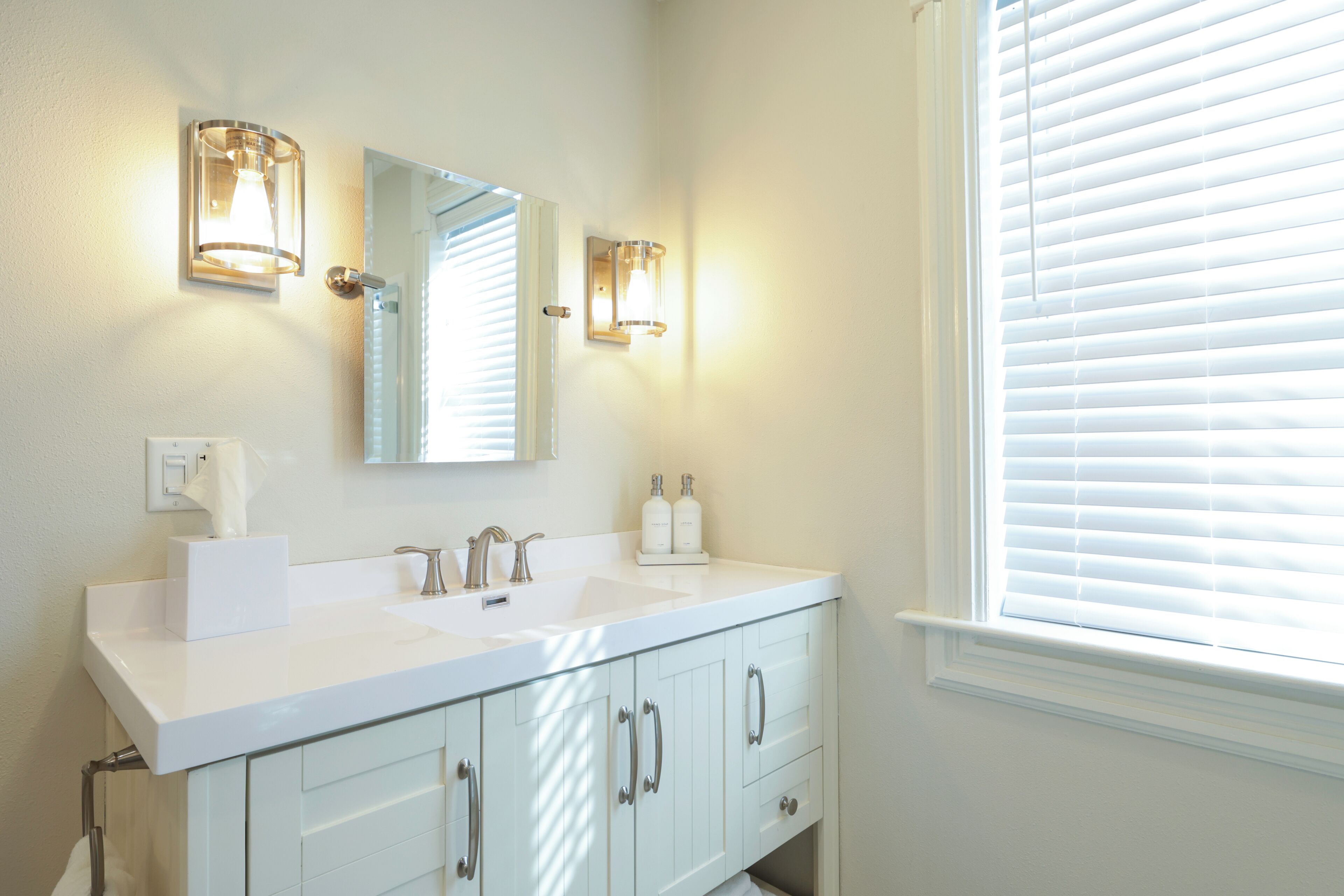 A bathroom with a white vanity, two sinks, a mirror, and wall sconces.