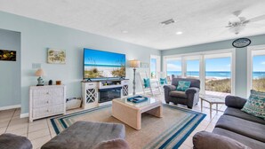 A living room with a large TV, a fireplace, a coffee table, and a view of the beach. - Belles Beach House (Panama City Beach)