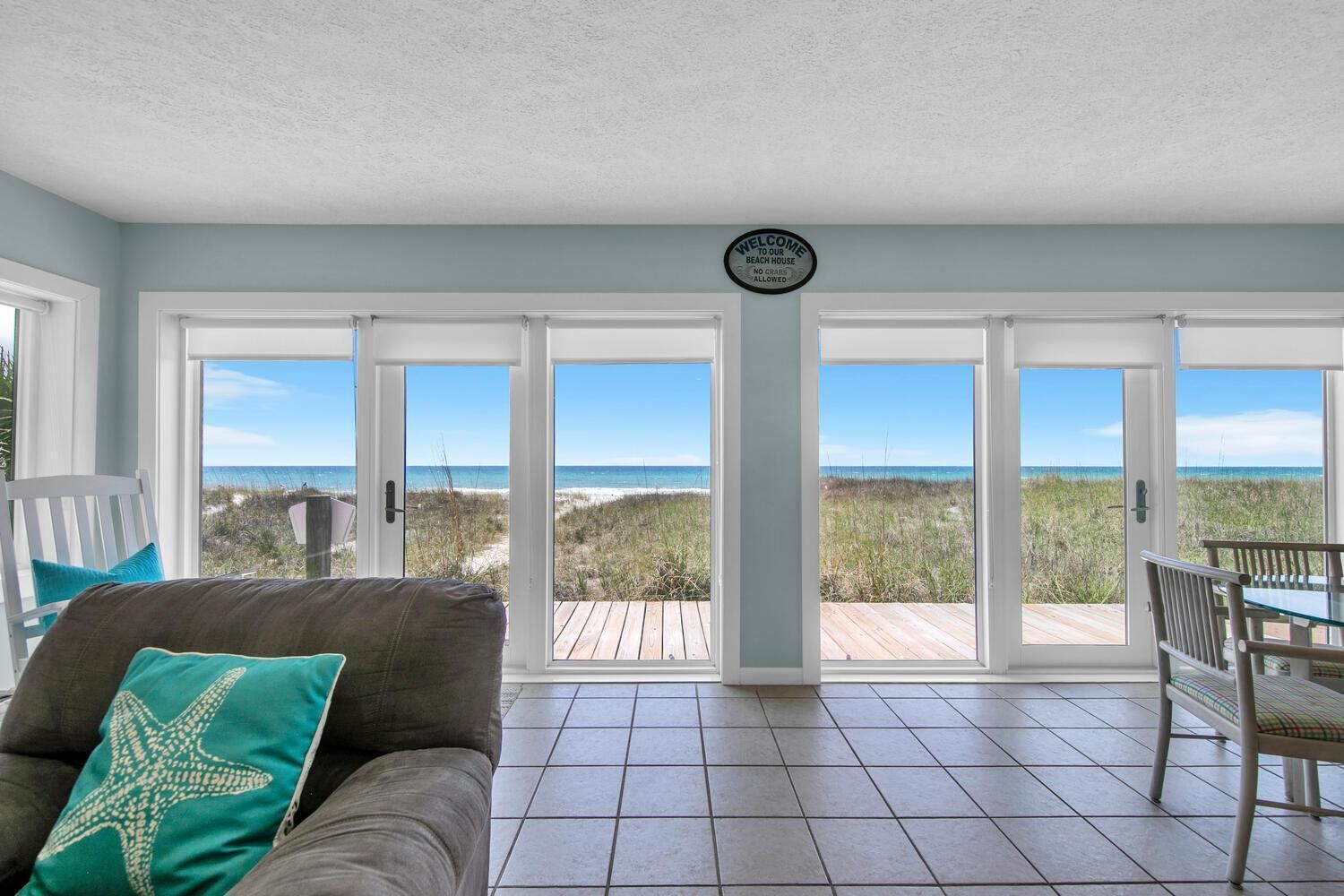A beach house interior with a large sliding glass door leading to a wooden deck overlooking the beach.