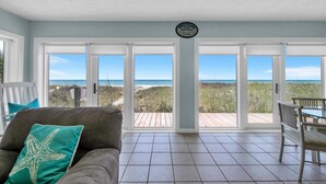 A beach house interior with a large sliding glass door leading to a wooden deck overlooking the beach. - Belles Beach House (Panama City Beach)