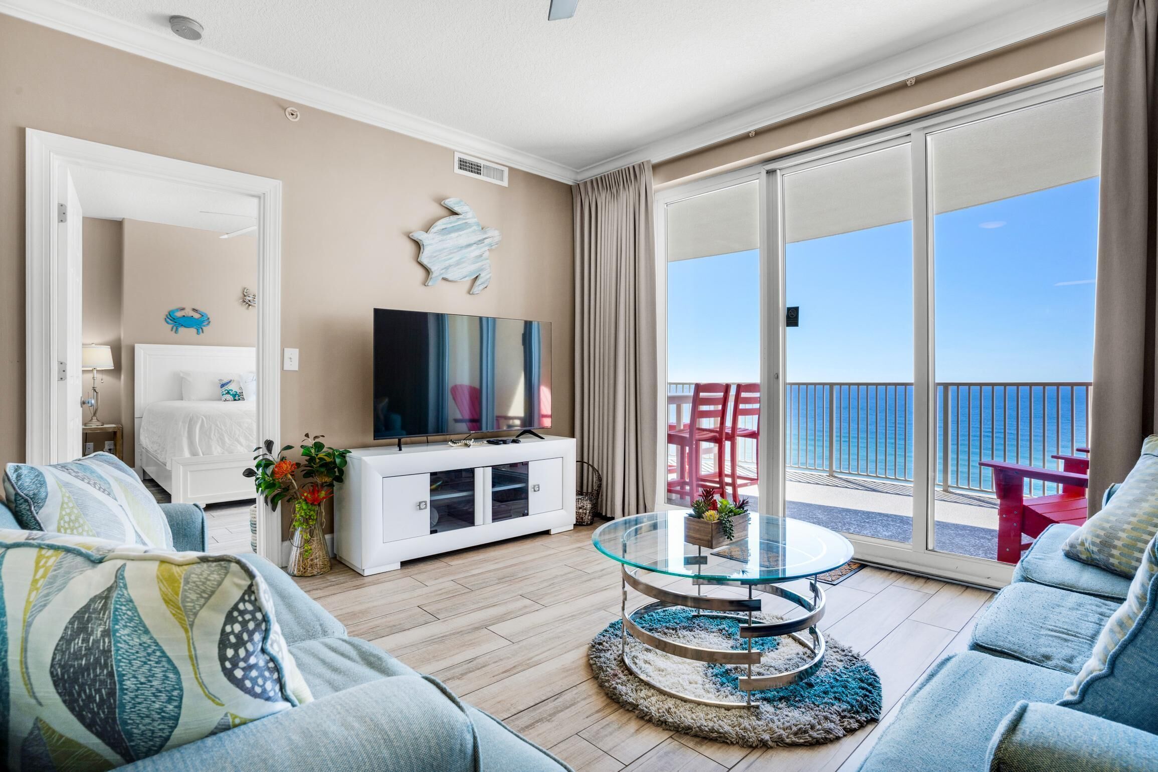A living room with a glass table, sofas, a TV, and a view of the ocean.