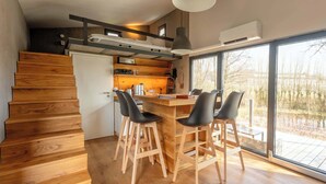 Una cocina moderna con pisos de madera, un comedor con taburetes, una escalera y ventanas grandes.