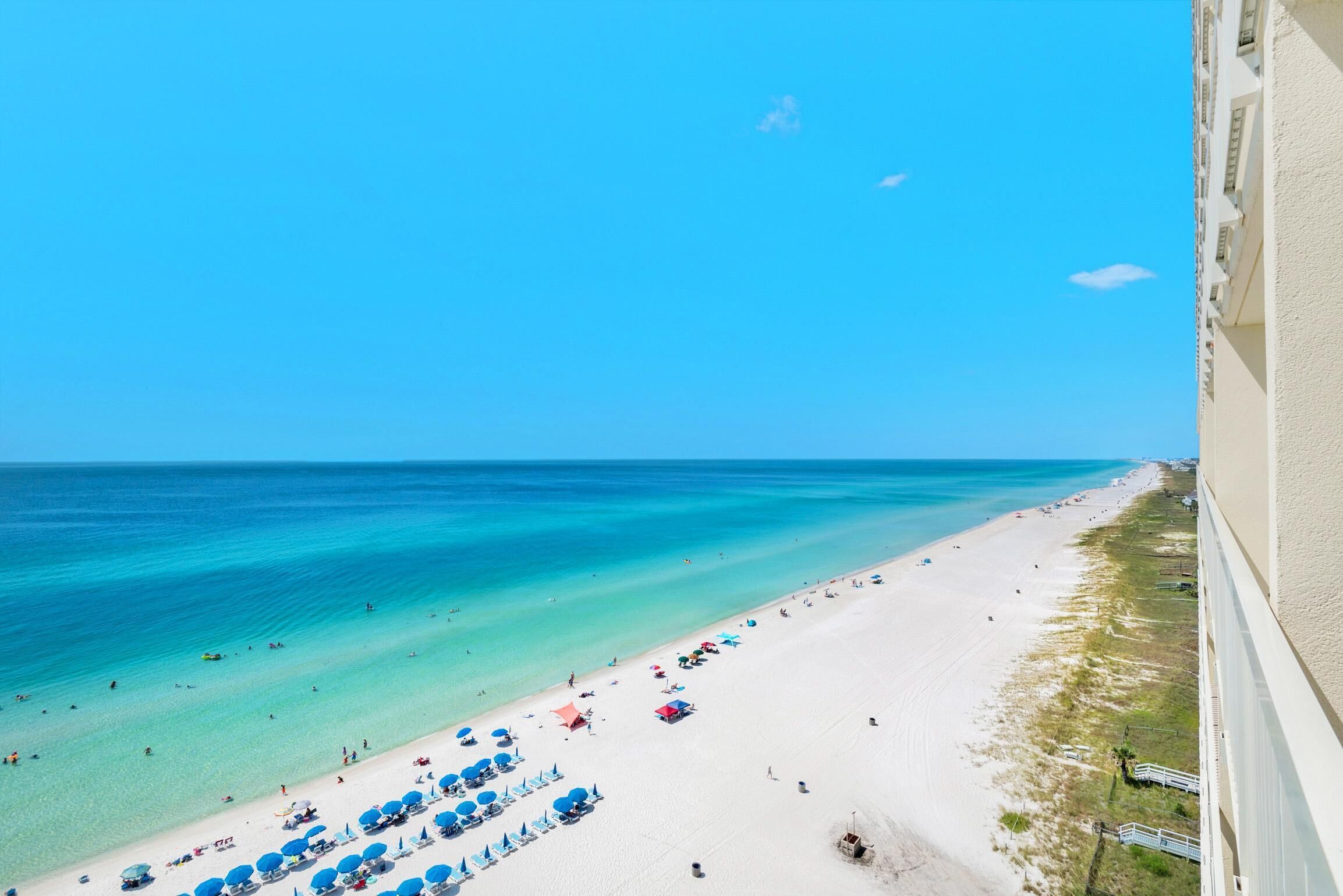 A beach with clear turquoise water, white sand, and blue umbrellas.