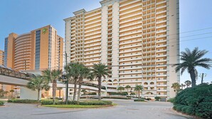 A high-rise hotel with multiple balconies, a covered walkway, and palm trees. - Celadon 1103 - Beach Paradise (Panama City Beach)