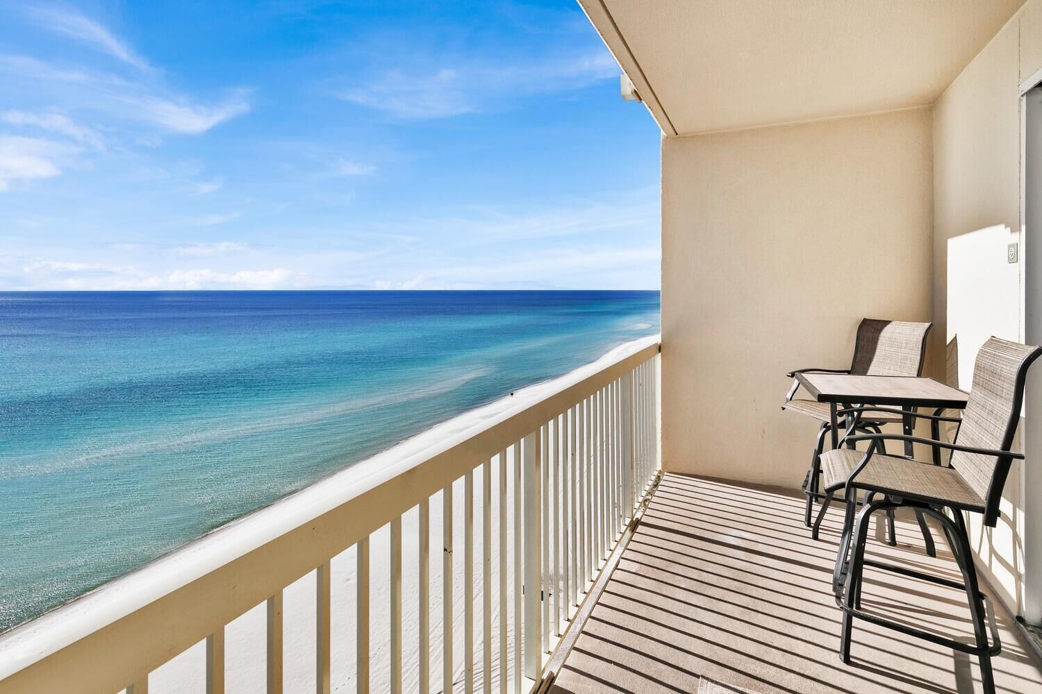 A balcony with a view of the ocean, a table, and two chairs.