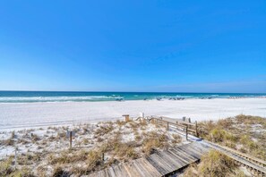 Ein Strand mit einer Holzpromenade, die zum Ufer führt, strahlend blauem Himmel und Wellen.