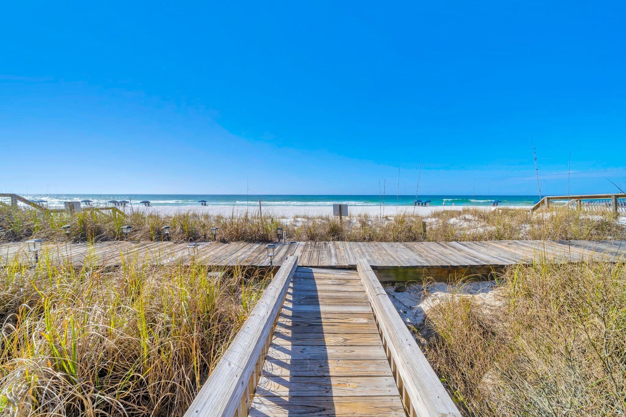 Ein hölzerner Steg führt zu einem Strand bei blauem Himmel.