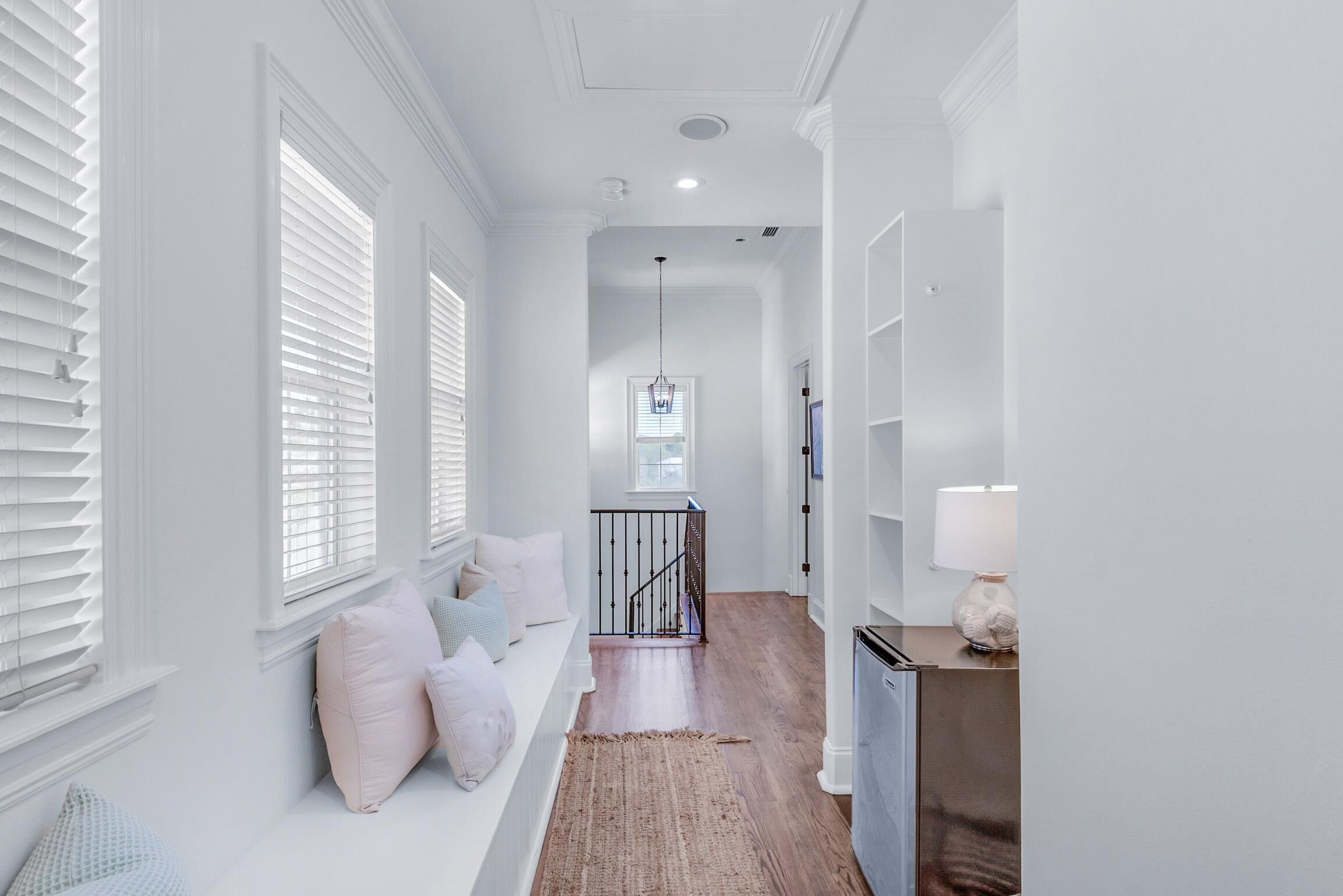A hallway with white walls, a wooden floor, a bench with pillows, a staircase, and a lamp.