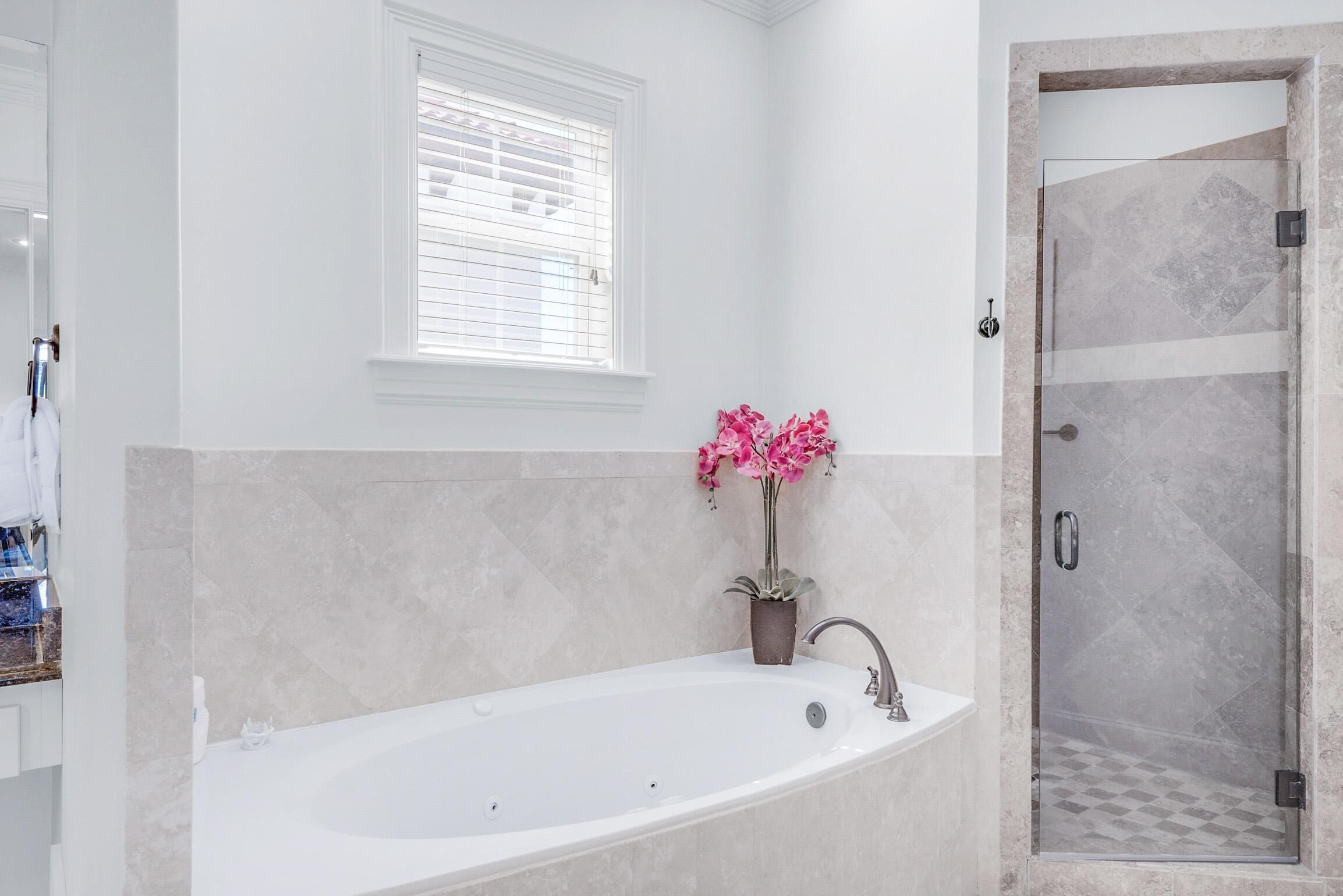 A modern bathroom with a freestanding bathtub, a glass shower enclosure, and a window with blinds.