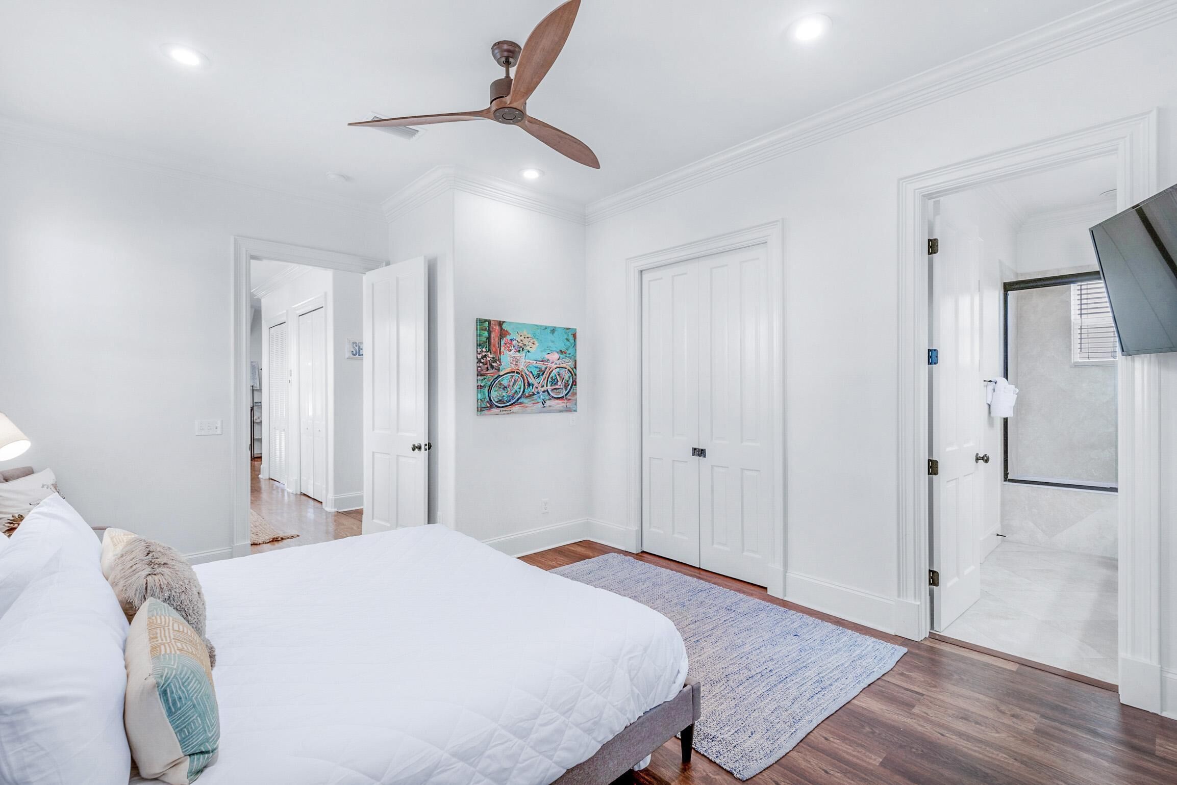 A bedroom with a bed, a ceiling fan, a painting, and a shower area.