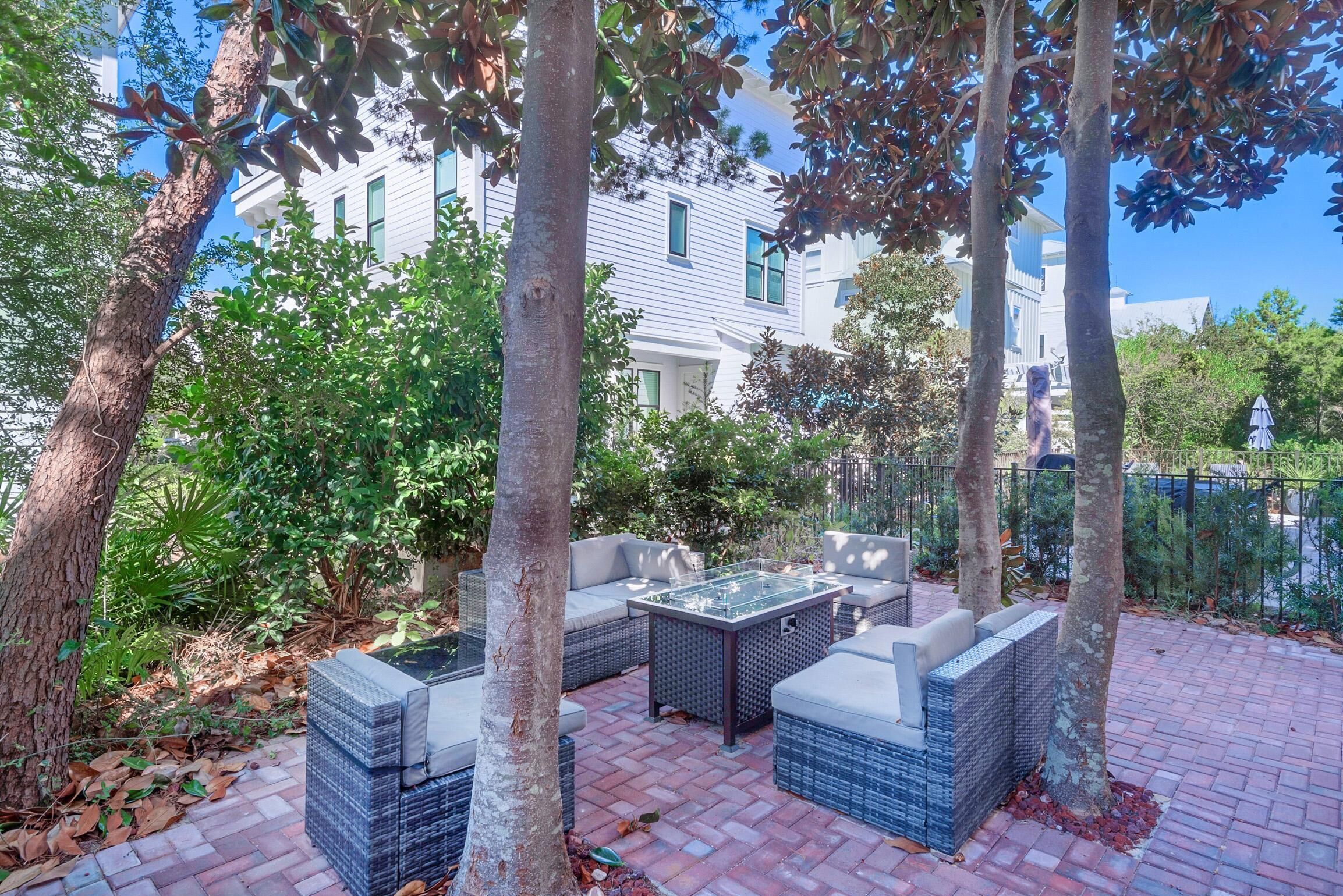 Un patio al aire libre con mobiliario de mimbre, una mesa de vidrio y piso de ladrillo.