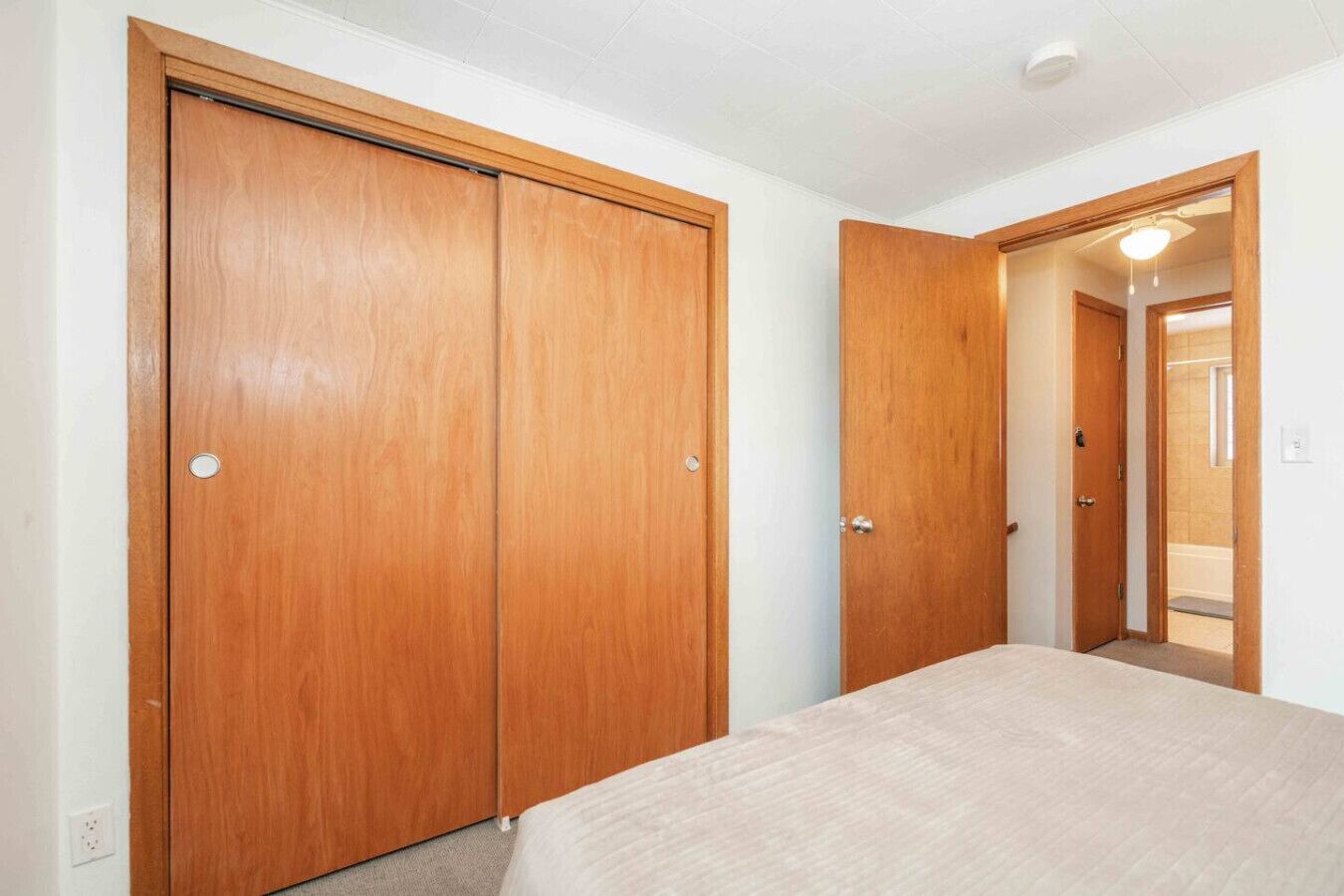 A bedroom with a bed, wooden wardrobe, and a bathroom visible through an open door.