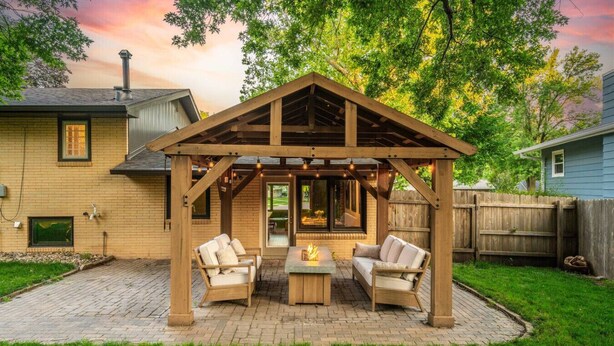 Una pérgola de madera con asientos y un brasero en un patio trasero.