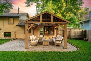 Eine Holz-Pergola mit Sitzgelegenheit und einem Feuerkorb in einem Garten.