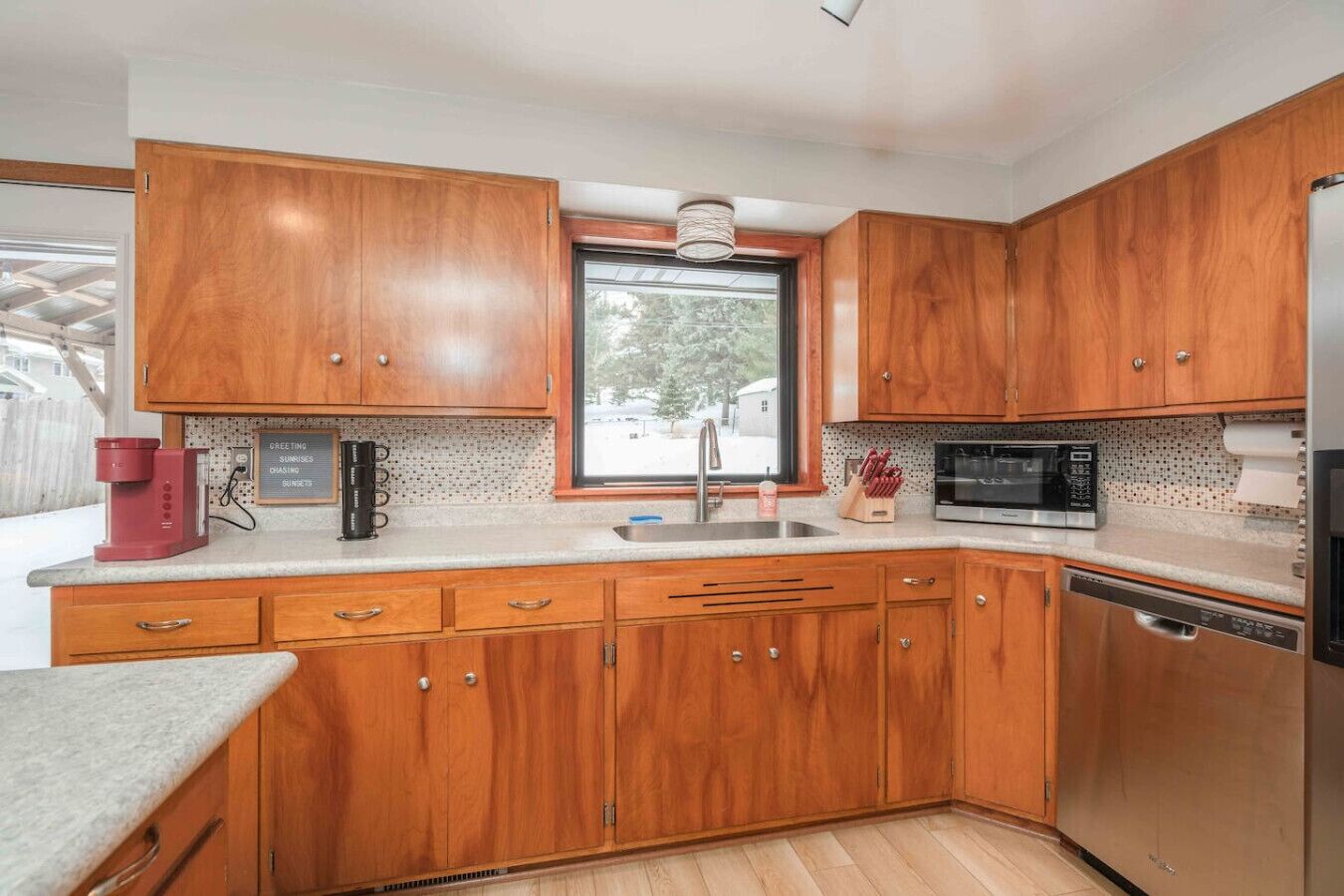 Una cocina con armarios de madera, un lavamanos de acero inoxidable, un microondas y una cafetera.