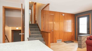 Una escalera con barandillas de madera y escalones alfombrados, una chimenea de piedra y una puerta con apliques de luz.