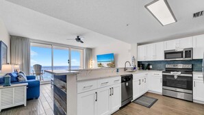 A modern kitchen with white cabinets, a microwave, oven, and dishwasher. There is a balcony with a view of the ocean. - Majestic Beach Towers 1-1014 (Panama City Beach)