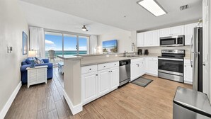 A modern kitchen with white cabinets, stainless steel appliances, and a view of the ocean. - Majestic Beach Towers 1-1014 (Panama City Beach)
