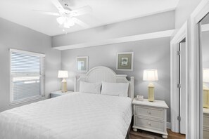 A bedroom with a bed, nightstands, a ceiling fan, and a window with blinds. - Majestic Beach Towers 2-803 (Panama City Beach)