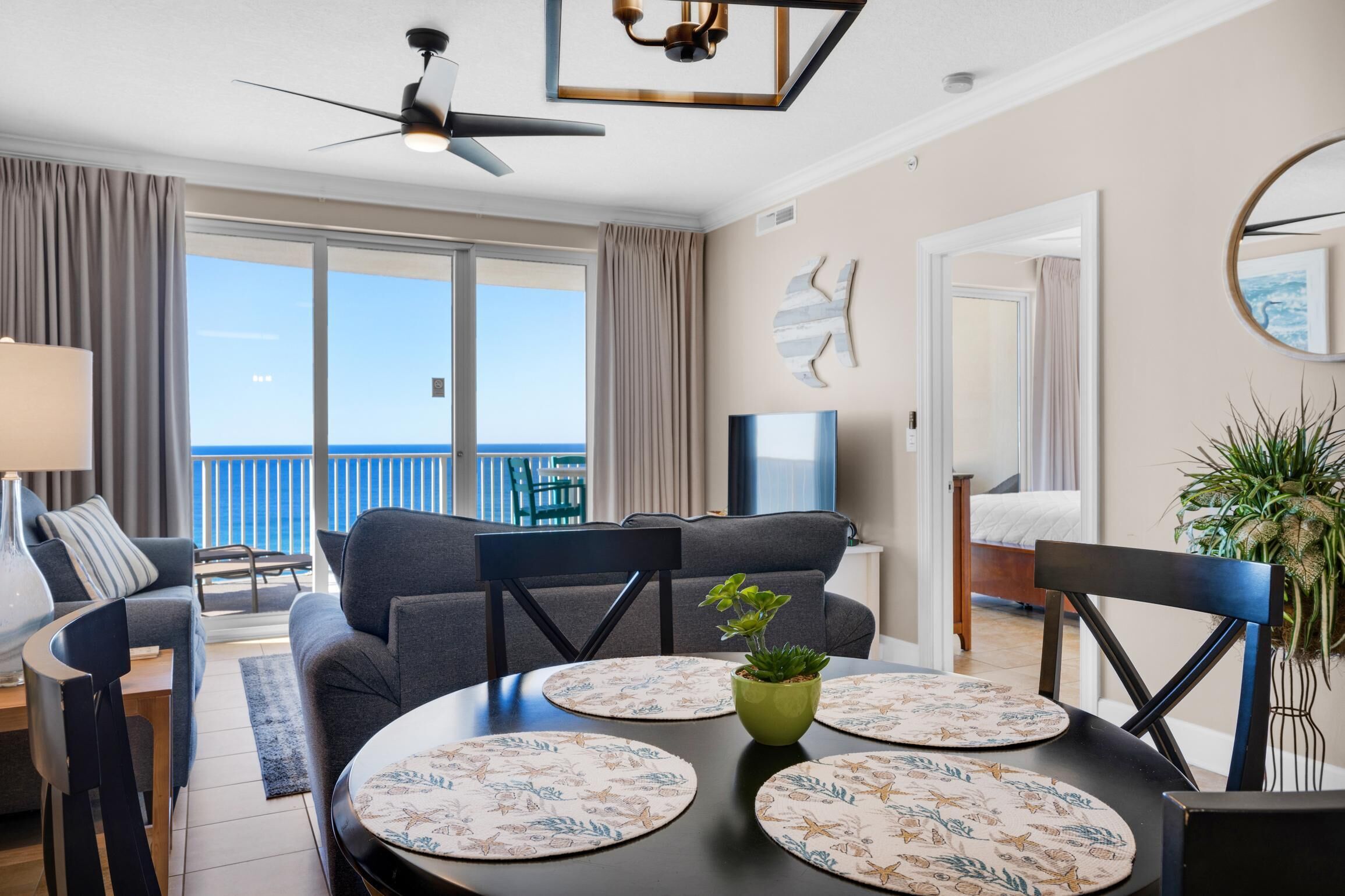Un salon moderne comprenant un canapé, des fauteuils, une table à manger avec des sets de table, un ventilateur de plafond, un téléviseur et un balcon avec vue.
