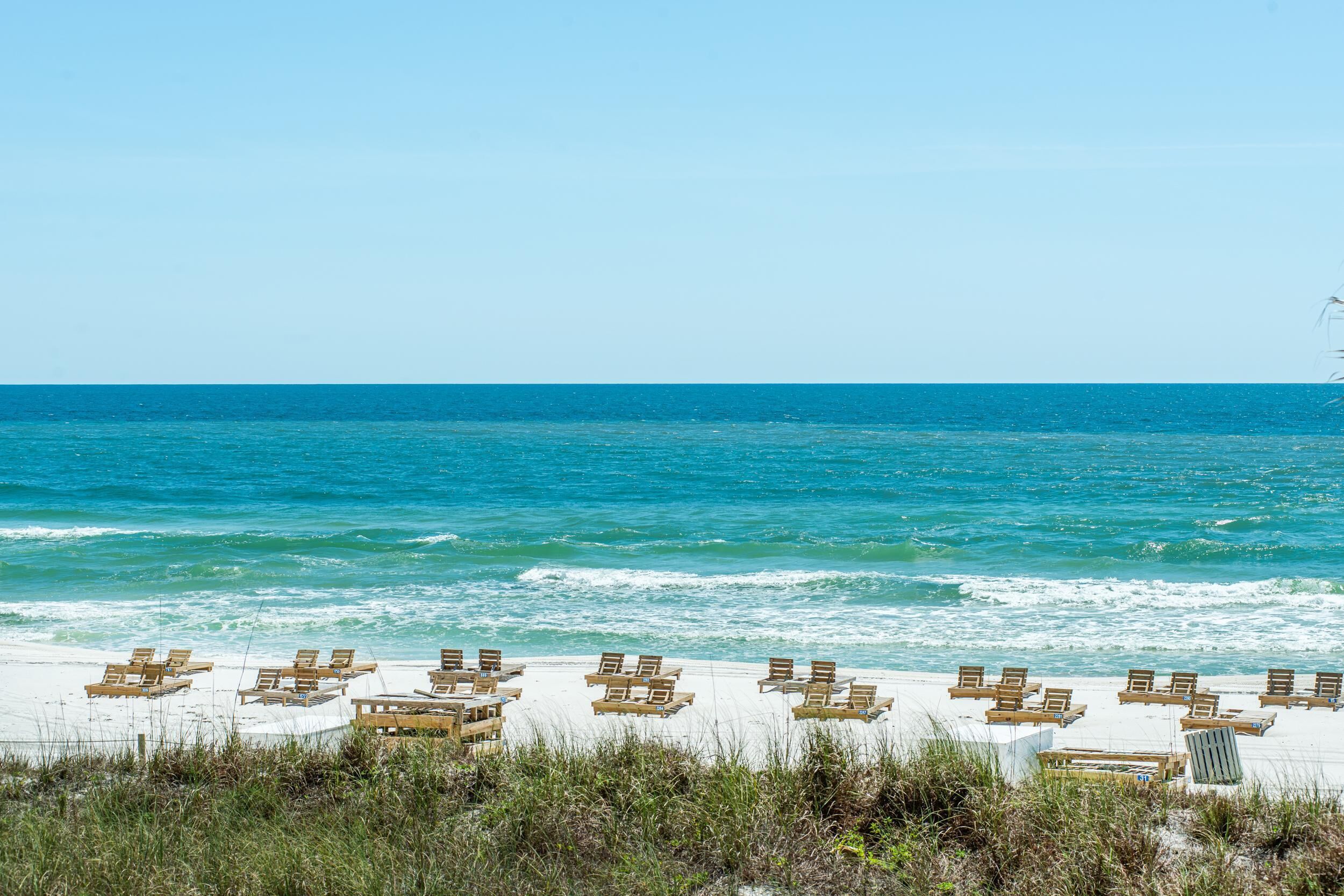 A beach with rows of wooden lounge chairs and tables facing the ocean.