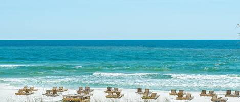 A beach with rows of wooden lounge chairs and tables facing the ocean.