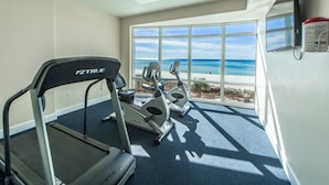 A gym with a treadmill, elliptical, and stationary bike, overlooking a beach.