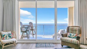 A balcony with a view of the ocean, wicker furniture, and a glass door.