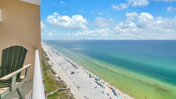 A beach with a clear view of the ocean and a chair on a balcony.
