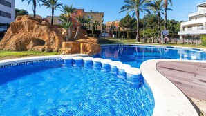Une piscine à l’eau d’un bleu cristallin, entourée de palmiers et bordée d’un relief rocheux.