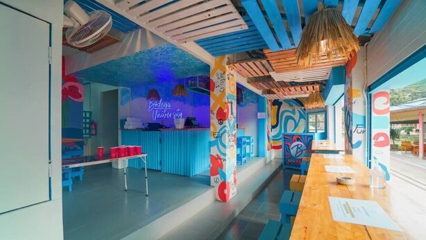 A vibrant, modern interior with a blue and white color scheme, featuring a long wooden table, blue seating, and a counter area. - Bodega Koh Phi Phi (Ko Phi Phi)
