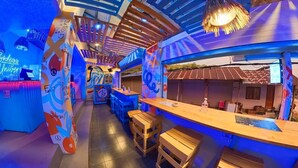 A vibrant bar area with wooden stools and a neon sign reading "Bodega University". - Bodega Koh Phi Phi (Ko Phi Phi)