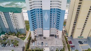 A high-rise hotel with a prominent logo, multiple floors, and a parking area in front.