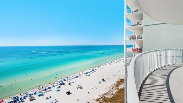 A beach view from a hotel balcony with a clear sky, a sandy beach, and a calm sea.