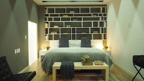 Een slaapkamer met een bed, nachtkastjes, een boekenkast en een bankje.