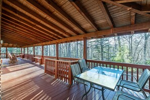 A covered outdoor deck with wooden railings, a glass table, and metal chairs.
