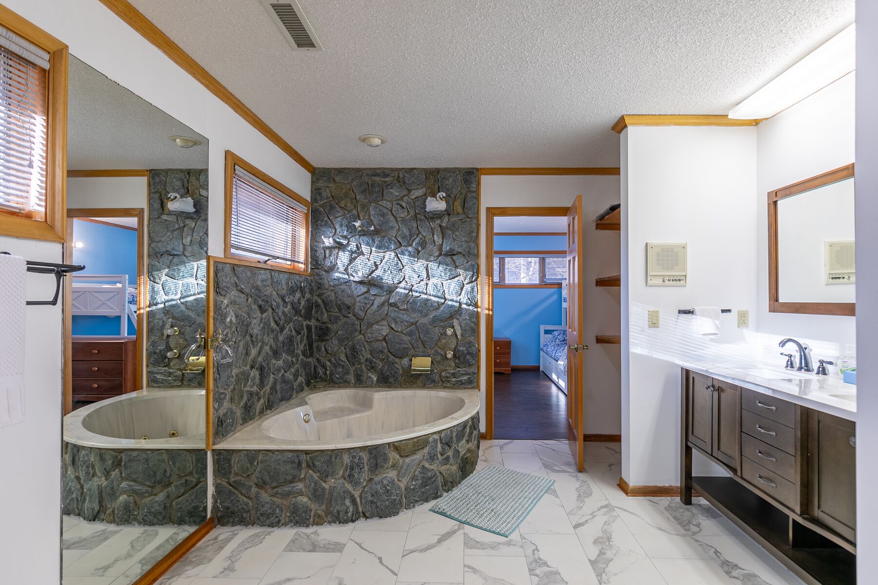 Un baño con pared de piedra, una bañera, un lavamanos y un espejo.