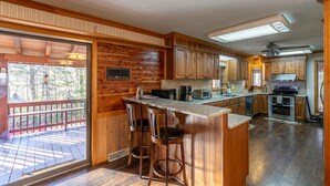A spacious kitchen with wooden cabinetry, a bar area with stools, and a large window overlooking a deck.