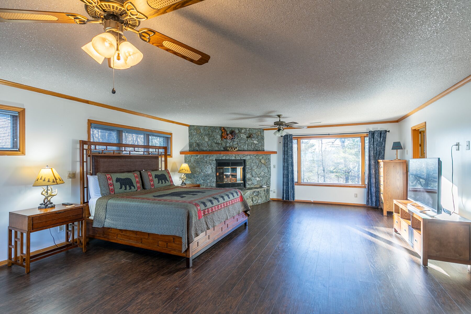 A spacious bedroom with a large bed, two bedside tables, a fireplace, and a ceiling fan.