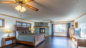 A spacious bedroom with a large bed, two bedside tables, a fireplace, and a ceiling fan.