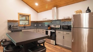 Eine moderne Küche mit Holzbalkendecke, einem Esstisch mit Hockern, einem Kühlschrank, einer Mikrowelle und einem Herd.