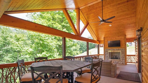 Eine Holzterrasse mit Tisch und Stühlen, einem Kamin aus Stein und einem Deckenventilator.