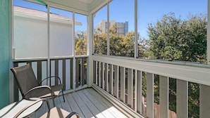 A covered outdoor balcony with two chairs and a table, wooden railings, and a view of trees and buildings. - Sand Castles West T24 (Panama City Beach)